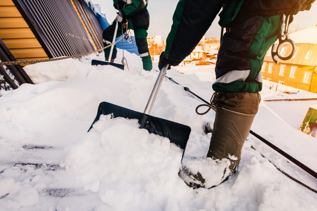 Zwei Mitarbeiter mit Schneeschaufeln entfernen Schnee von einem Grundstück