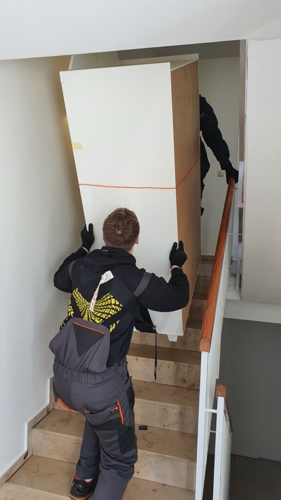 Mitarbeiter von Martens Services tragen einen Schrank durch ein Treppenhaus